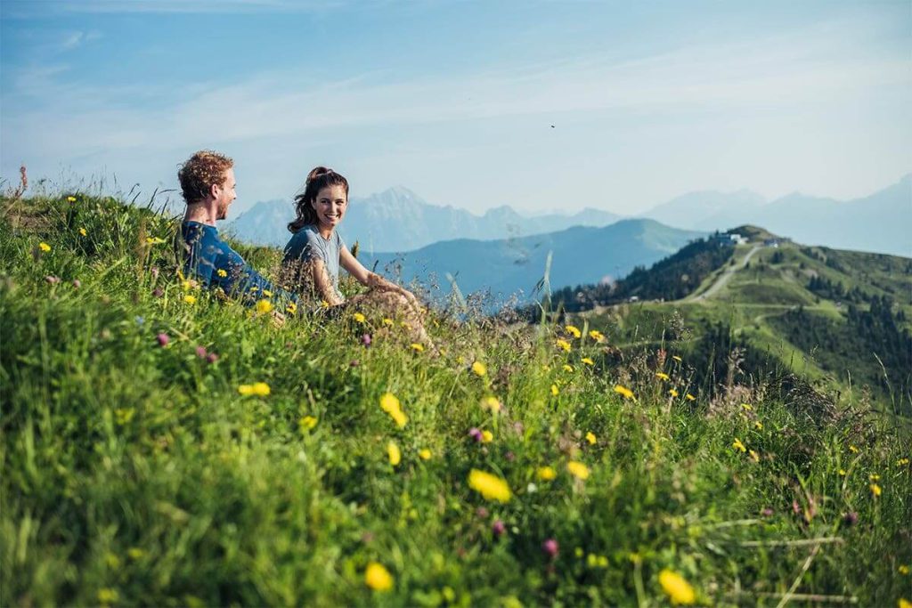 Ontspannend stel op een weide met uitzicht op de bergen in Zell am See-Kaprun, bloeiende natuur eromheen.