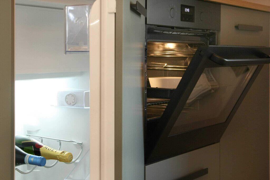 Küchenzeile mit Öffnung eines Backofens und Flasche Wein im Kühlschrank.