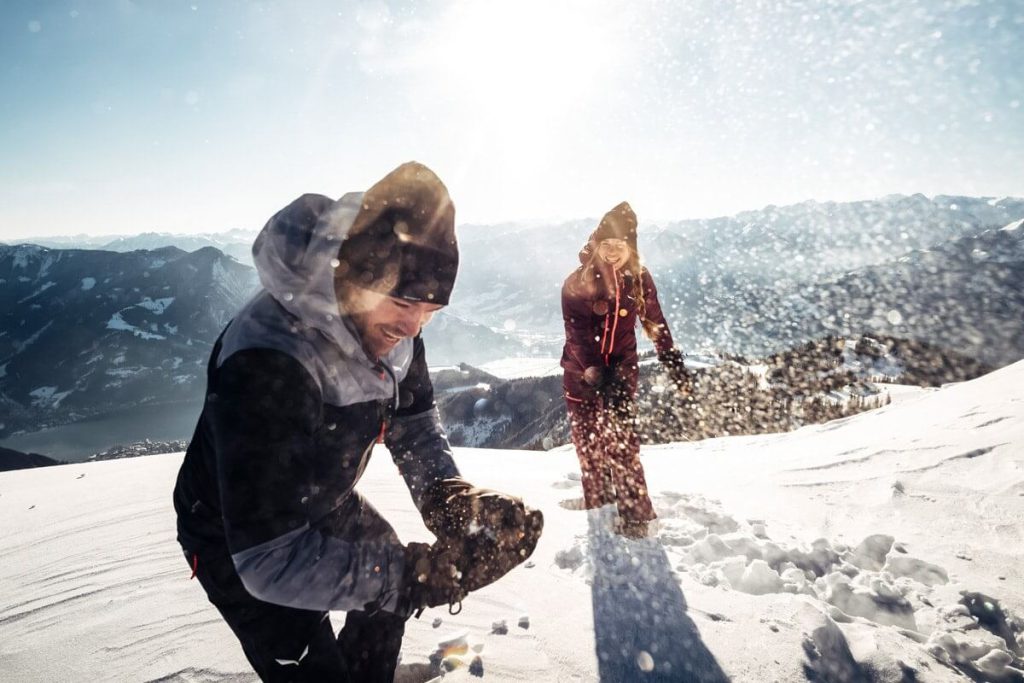 Aktivurlaub in Zell am See: Paar spielt im Schnee mit Bergblick und Sonnenschein.