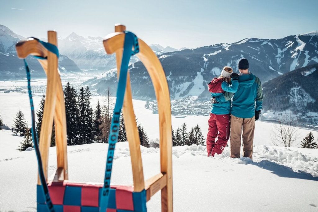 Paar genießt den Blick auf Zell am See und die Alpen von einem schneebedeckten Hang aus.
