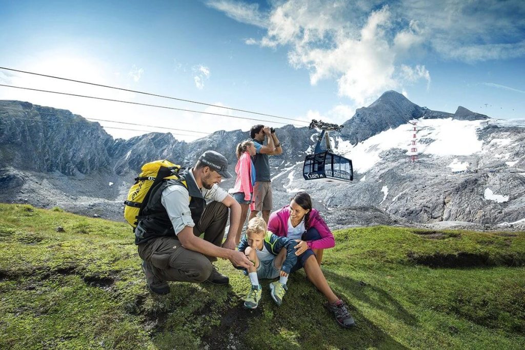 Familie beim Wandern in den Alpen mit Bergblick und Gondel im Hintergrund.