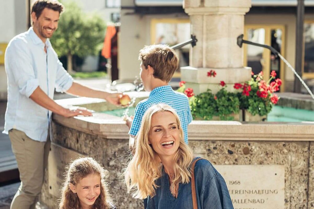 Familie am Brunnen in Zell am See, genießen die Zeit mit fröhlichen Momenten und Natur.