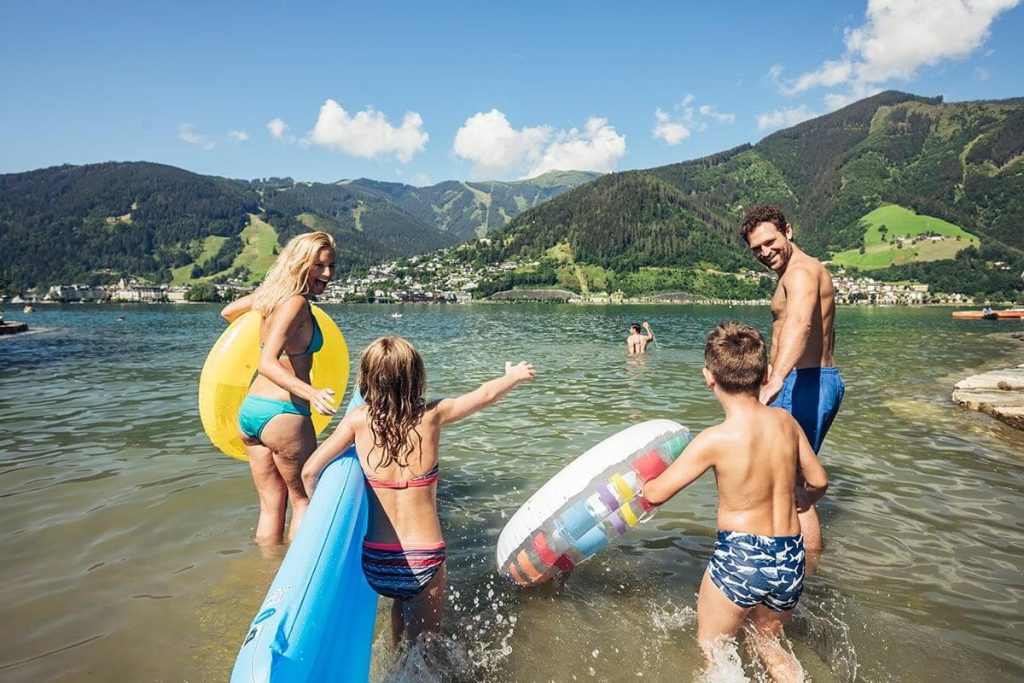 Familie im Wasser mit Schwimmreifen, umgeben von den Bergen Zell am Sees bei Sonnenschein.