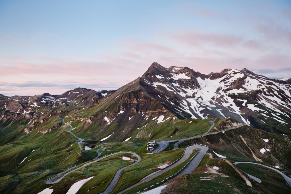 Serpentine road through green alpine landscape with snow-covered mountains