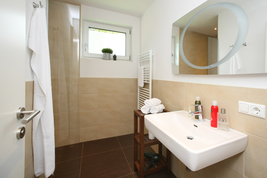 Světlá koupelna v apartmánu D s umyvadlem, velkým zrcadlem, sprchou, ručníky a oknem