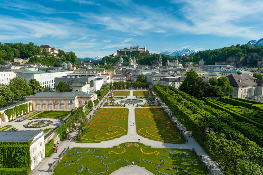 View across a baroque garden of a historic old town with fortress and mountains in the background